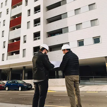 Due tecnici edili osservano un progetto davanti a un edificio residenziale con dati: 20K+ sinistri, 13 servizi, 3 target